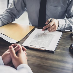a person talking to someone across him while discussing a set of documents and holding a pen